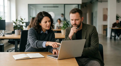 Two employees reviewing information on a laptop during an AI ethics and workplace compliance discussion.